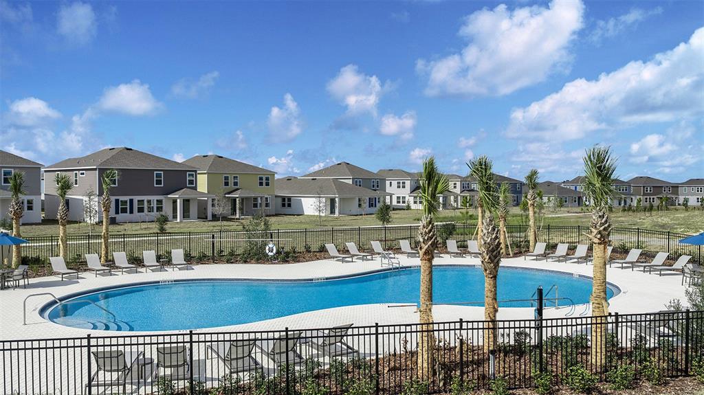 A community swimming pool with lounge chairs is surrounded by a black fence and houses — 241 STREAMWATER WAY, GROVELAND, FL