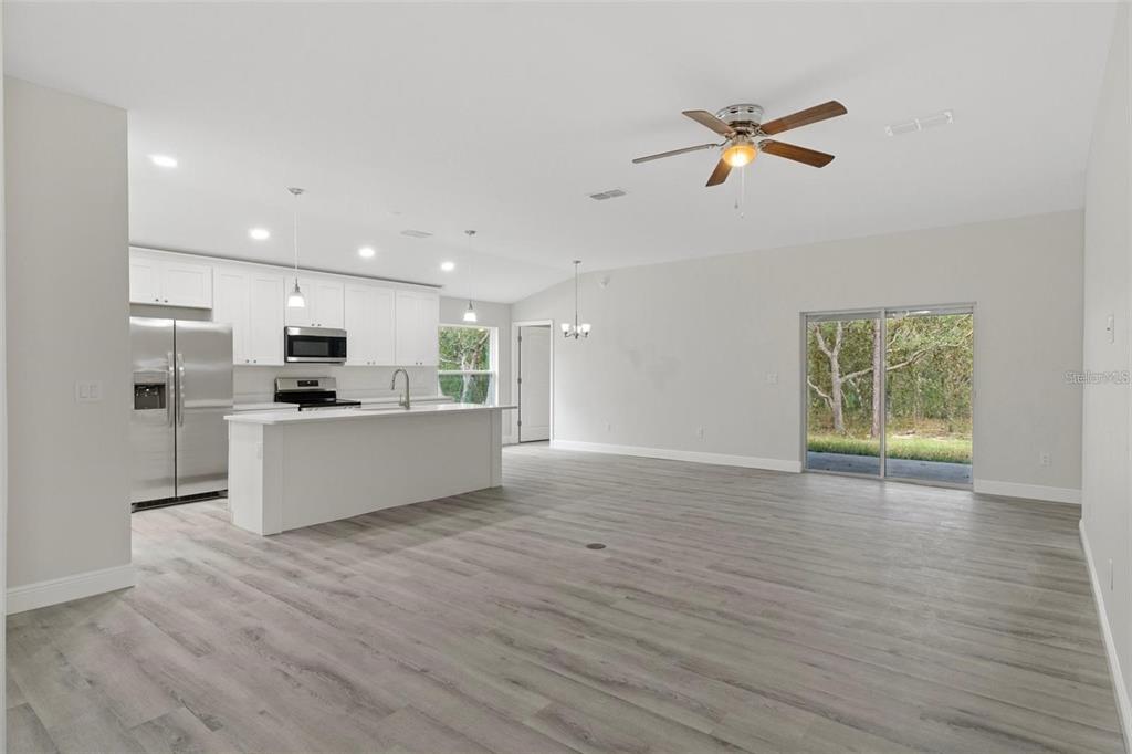 An open-concept kitchen and living area features white cabinetry, stainless steel appliances, and wood-look flooring — 3248 E PORTER STREET, INVERNESS, FL