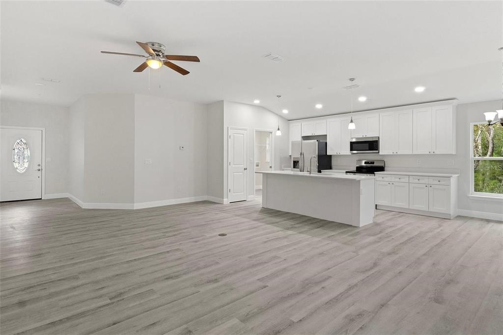 An open-concept kitchen and living area features white cabinetry, a kitchen island, and wood-look flooring — 3248 E PORTER STREET, INVERNESS, FL