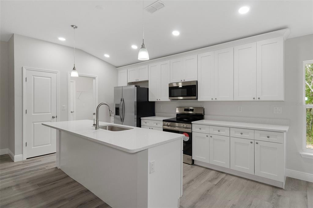 A modern kitchen features white cabinets, stainless steel appliances, a center island, and wood-look flooring — 3248 E PORTER STREET, INVERNESS, FL