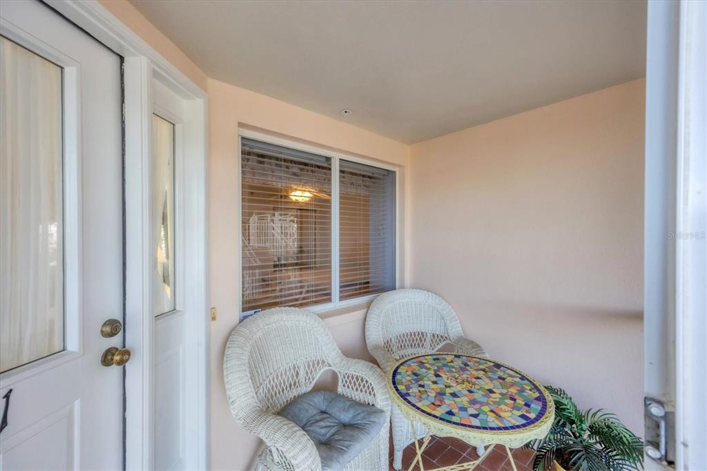 A small covered balcony features two white wicker chairs and a colorful mosaic-topped table — 11000 PLACIDA ROAD UNIT 1801, PLACIDA, FL