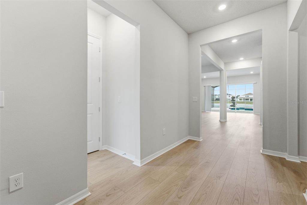 A hallway with light wood-look flooring leads toward an open living area with sliding doors — 8369 FENTON STREET, ORLANDO, FL