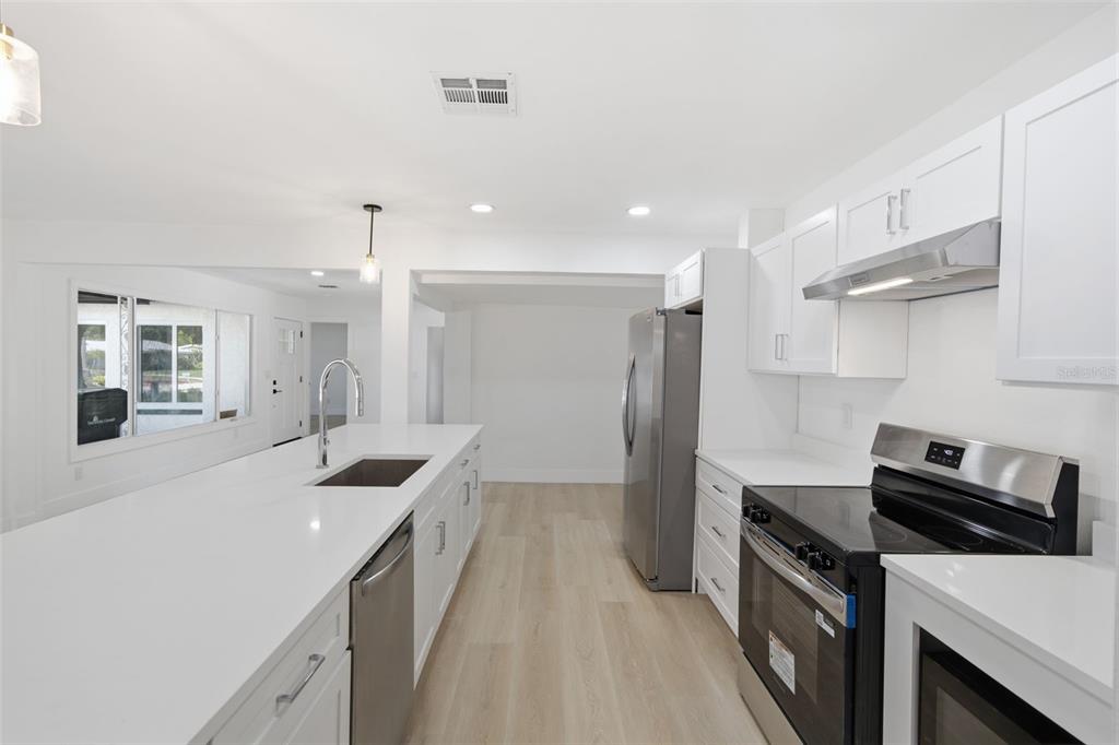 A modern kitchen features white cabinetry, quartz countertops, stainless steel appliances, and light wood flooring — 2317 GROVE STREET, SARASOTA, FL