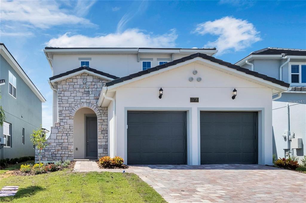 A two-story house exterior with a stone-accented entryway, a two-car garage, and landscaped front yard — 15730 VETTA DRIVE, MONTVERDE, FL