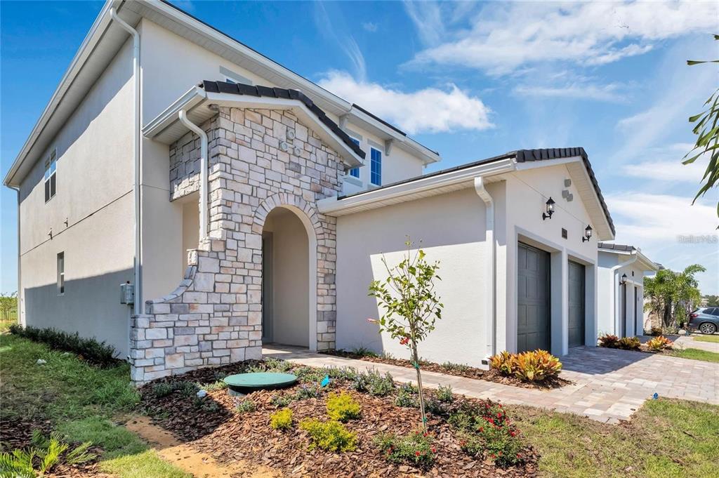 A stone-faced arched entryway leads to a gray front door with a paver walkway — 15730 VETTA DRIVE, MONTVERDE, FL