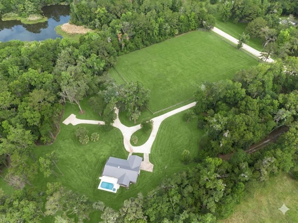 A black metal gate sits between two stone pillars at the entrance to a driveway — 14810 NW 185 STREET, WILLISTON, FL