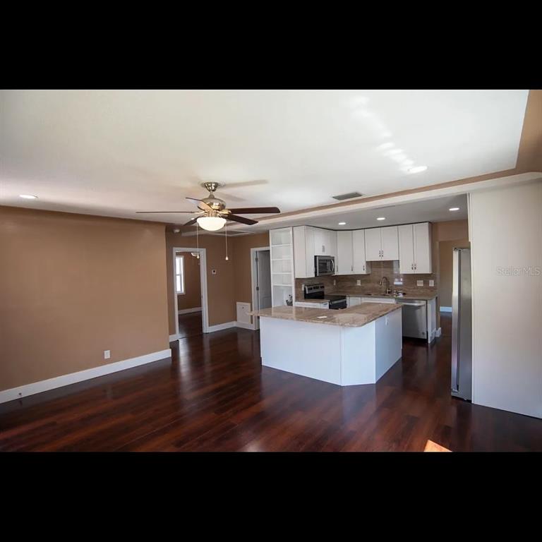 An open-concept kitchen with white cabinets and a granite island overlooks a hardwood-floored living area — 1329 34TH AVENUE N, ST PETERSBURG, FL