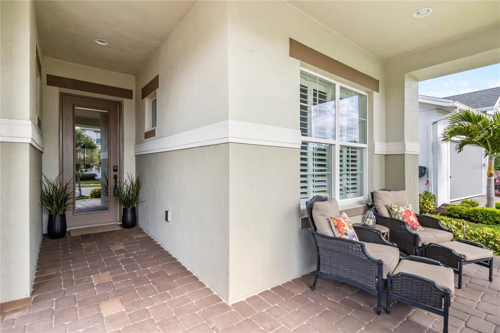A covered front porch features a glass-paneled door, paver flooring, and two outdoor chairs — 2748 GREENLANDS STREET, ST CLOUD, FL