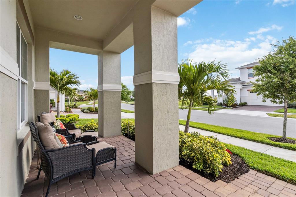 A covered front porch with brick pavers, two outdoor chairs, and views of a neighborhood street — 2748 GREENLANDS STREET, ST CLOUD, FL