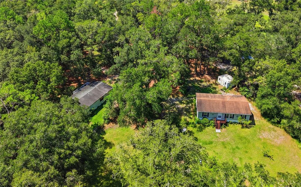 An aerial view shows two houses nestled among dense trees on a grassy lot — 24662 NW 84TH PLACE, ALACHUA, FL