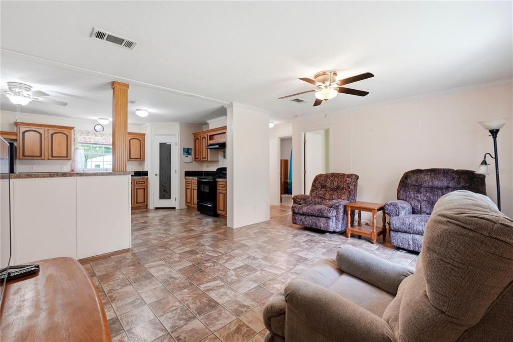 A living room with tile flooring opens into a kitchen with wood cabinets and appliances — 24662 NW 84TH PLACE, ALACHUA, FL