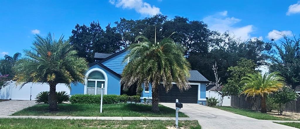 A blue single-story house with a two-car garage and three palm trees in the front yard — 8070 VILLAGE GREEN ROAD, ORLANDO, FL