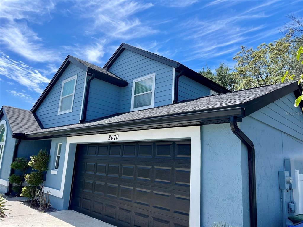 A two-story house with blue siding, a dark garage door, and a black shingled roof — 8070 VILLAGE GREEN ROAD, ORLANDO, FL