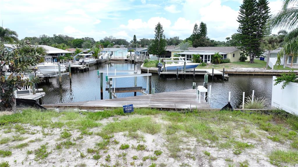 A wooden dock with a boat lift sits on a canal behind a grassy lot — 303 MORNINGSIDE DRIVE, PALM HARBOR, FL