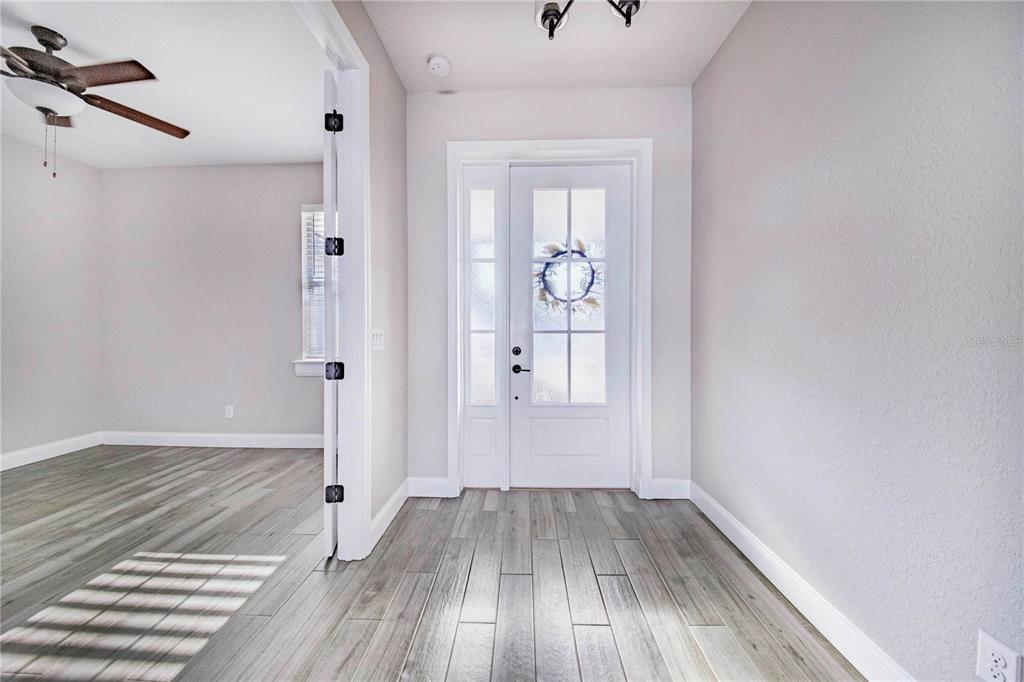 A bright entryway features light wood-look flooring, white walls, and a glass-paneled front door — 5017 RIDGEFIELD LANE, LAKELAND, FL