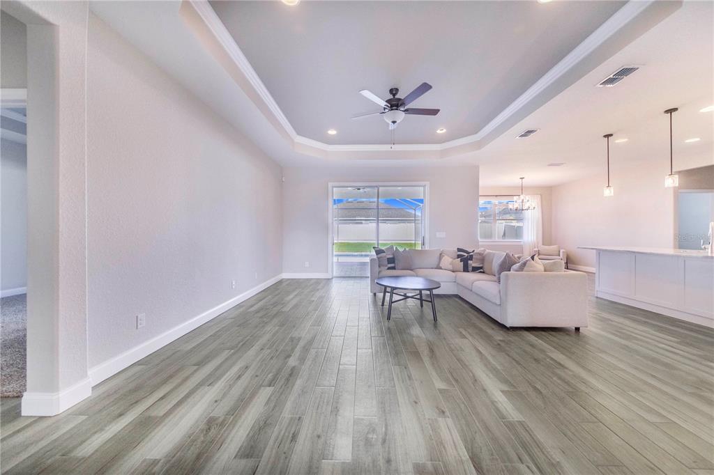 A spacious living room features light wood-look flooring, a tray ceiling, and a sectional sofa — 5017 RIDGEFIELD LANE, LAKELAND, FL