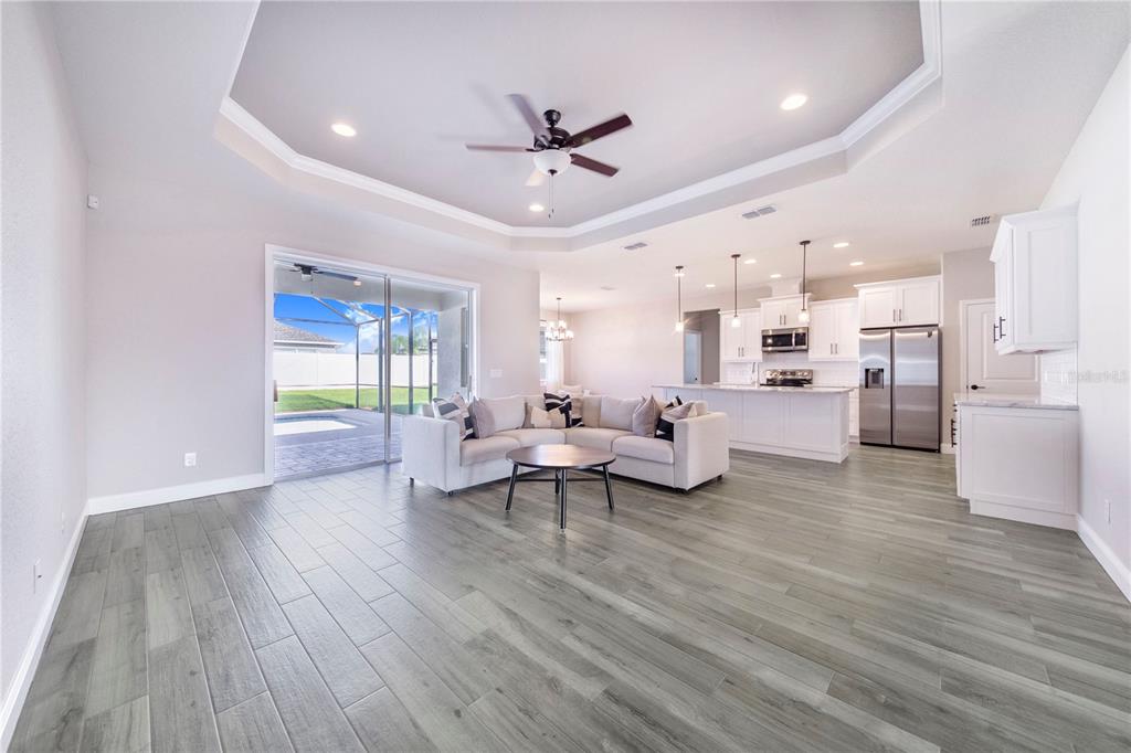 An open-concept living room and kitchen with gray wood-look tile flooring and a tray ceiling — 5017 RIDGEFIELD LANE, LAKELAND, FL