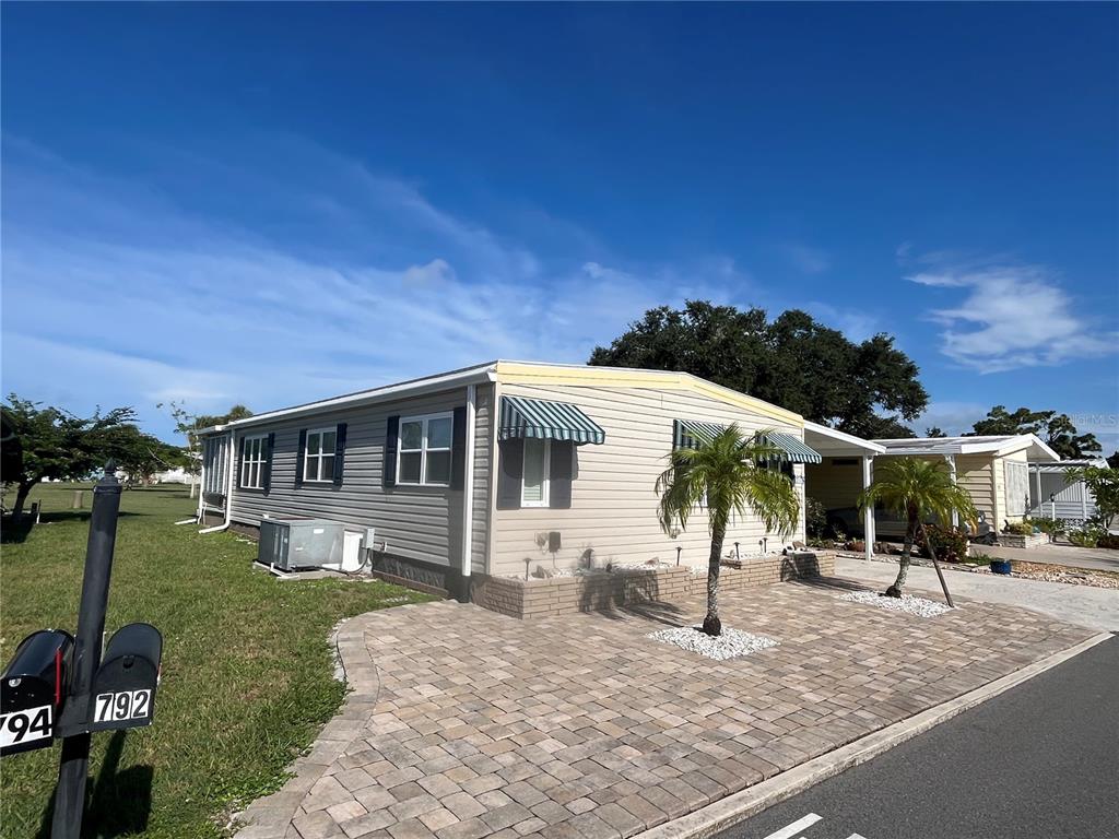 A single-story manufactured home features light siding, green striped awnings, and a brick paver patio — 792 GRADO DRIVE, VENICE, FL