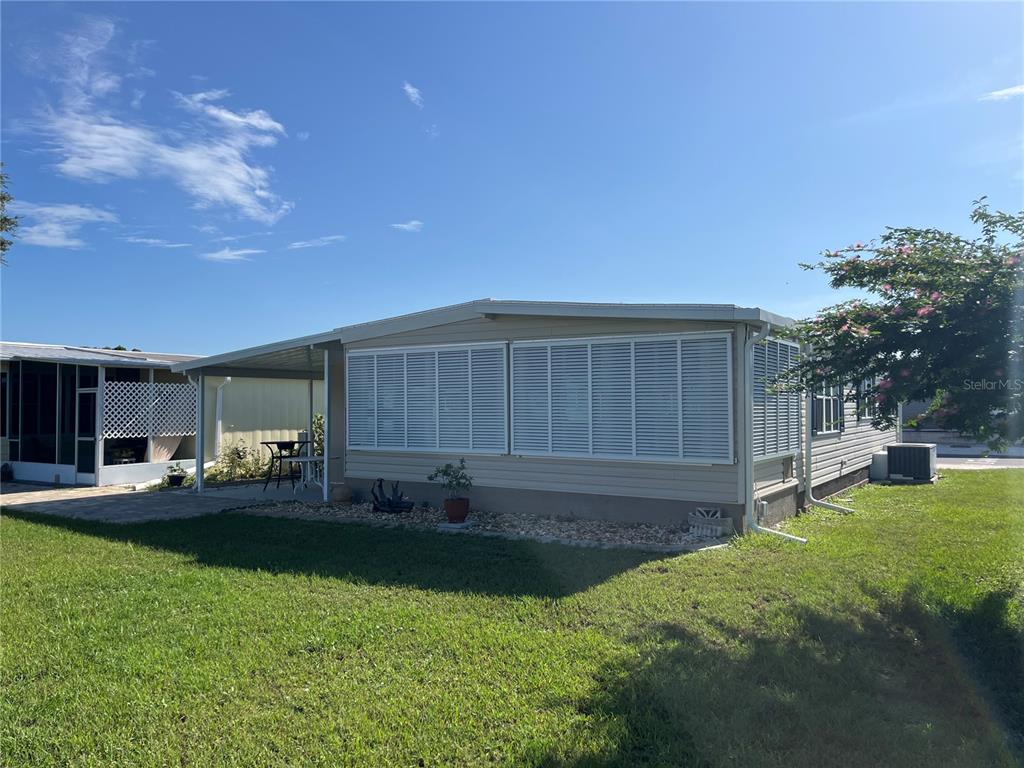 A single-story manufactured home with a carport and white louvered shutters on a sunny day — 792 GRADO DRIVE, VENICE, FL
