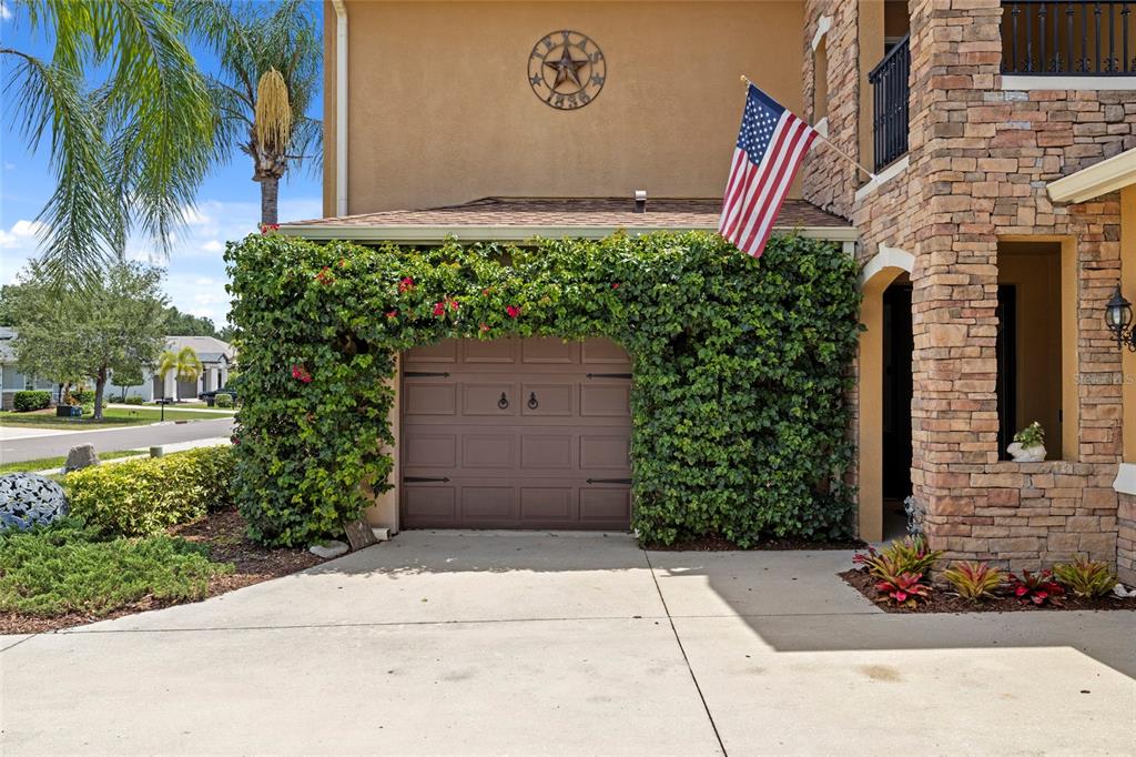 A brown garage door is framed by lush green vines and topped with an American flag — 2351 123RD PLACE E, PARRISH, FL