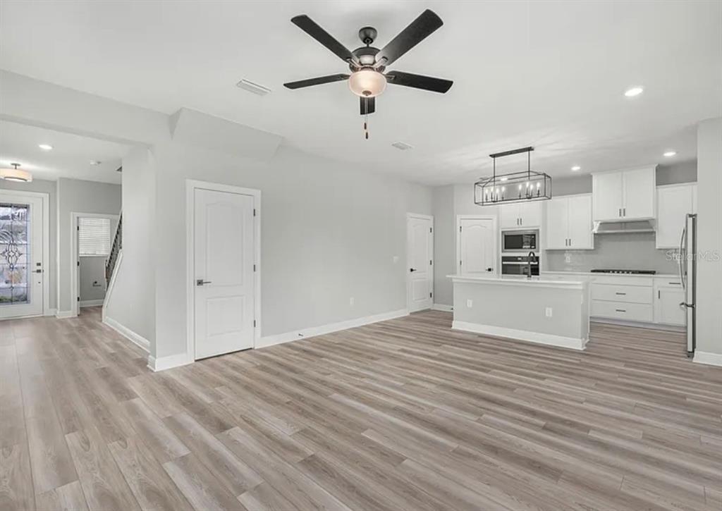 An open-concept kitchen and living area features light gray walls, wood-look flooring, and white cabinetry — 1399 GREENFIELD LOOP, KISSIMMEE, FL