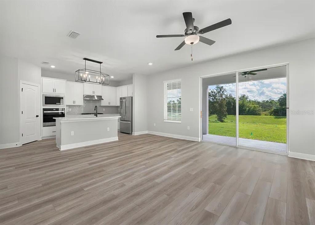 A bright open-concept kitchen and living area featuring light wood flooring and a sliding glass door — 1399 GREENFIELD LOOP, KISSIMMEE, FL