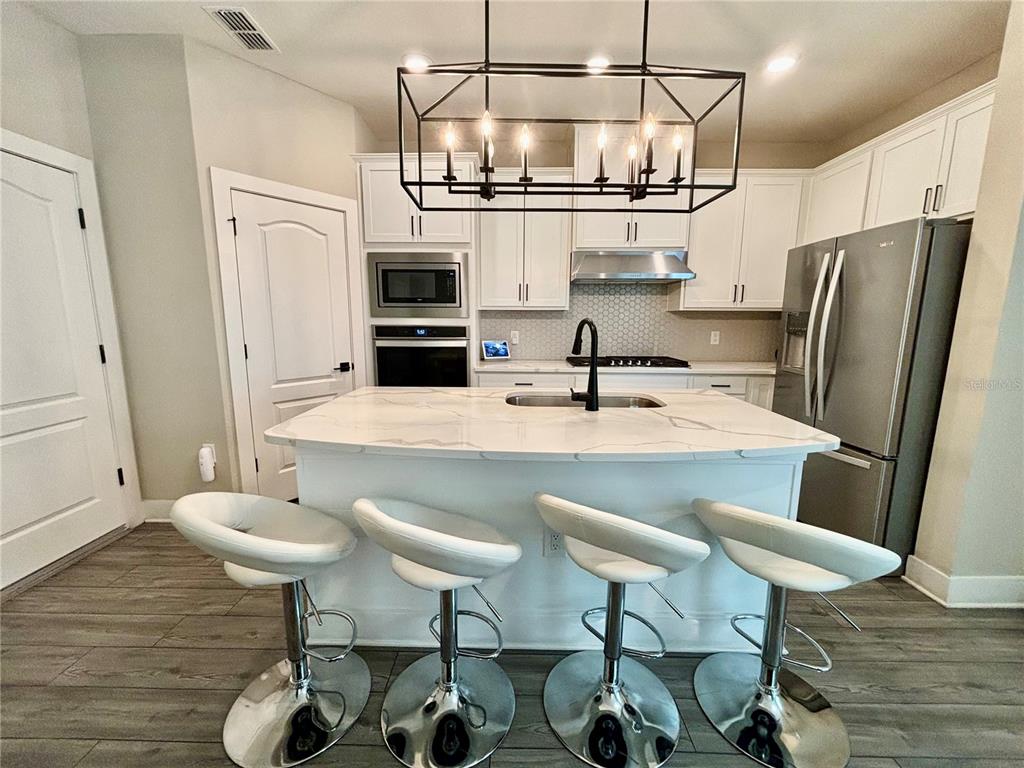 A kitchen features a white marble island with four bar stools and stainless steel appliances — 1399 GREENFIELD LOOP, KISSIMMEE, FL