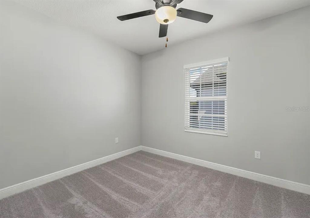 An empty bedroom features light gray walls, gray carpeting, a ceiling fan, and a window — 1399 GREENFIELD LOOP, KISSIMMEE, FL