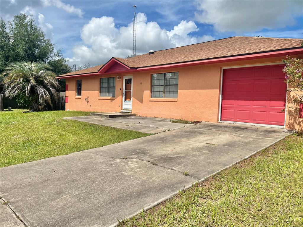 A single-story peach-colored house features a red garage door and a concrete driveway — 16 OAK PASS LOOP, OCALA, FL