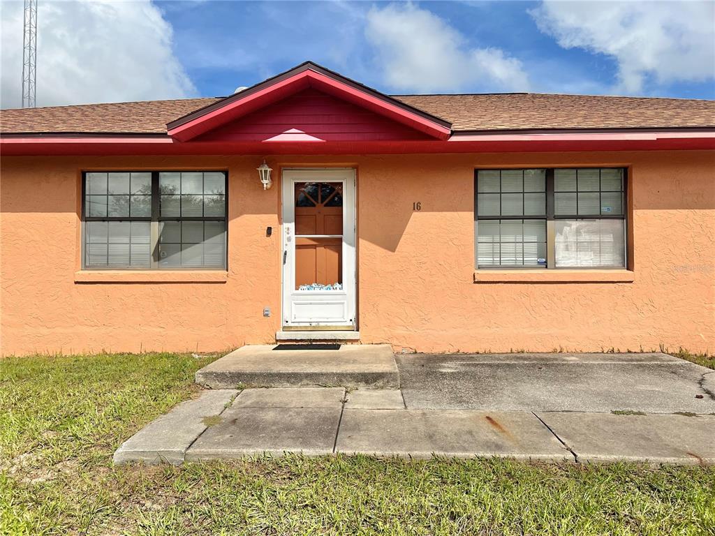 The exterior of a single-story house with peach-colored stucco walls and a brown shingled roof — 16 OAK PASS LOOP, OCALA, FL