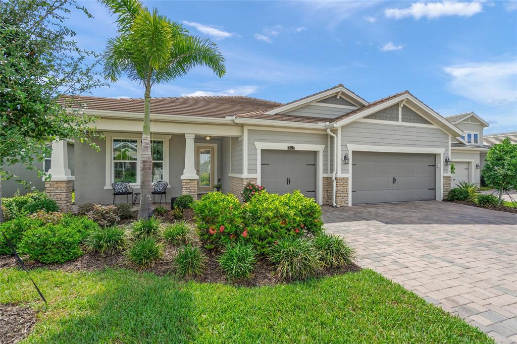 A single-story house with a gray exterior, stone accents, and a paved driveway — 5773 LONG SHORE LOOP, SARASOTA, FL