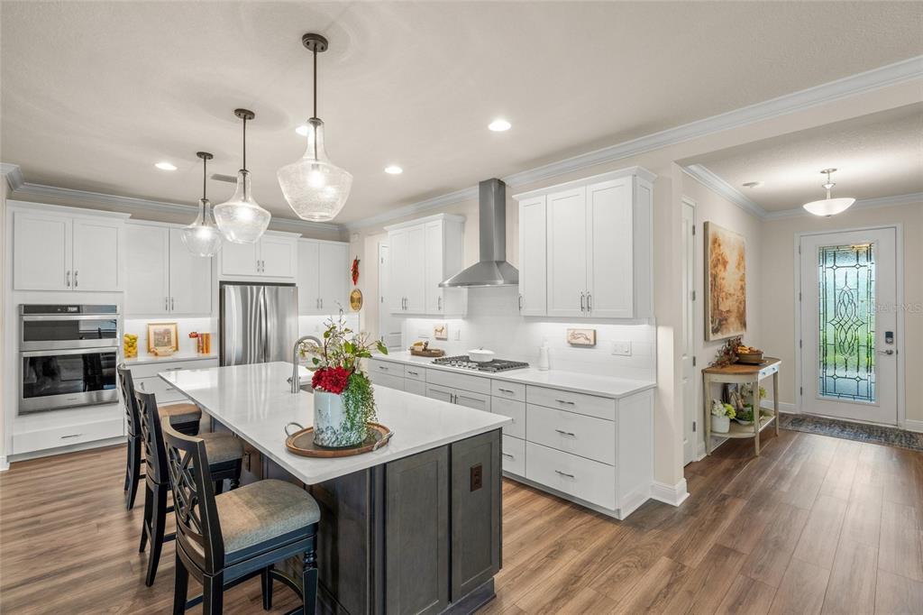 A modern white kitchen features a dark gray island, stainless steel appliances, and wood flooring — 5773 LONG SHORE LOOP, SARASOTA, FL