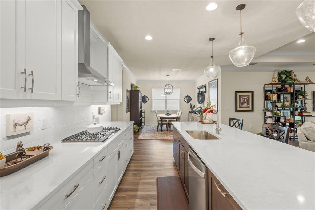 A modern kitchen features white upper cabinets, a large island with a sink, and wood-look flooring — 5773 LONG SHORE LOOP, SARASOTA, FL