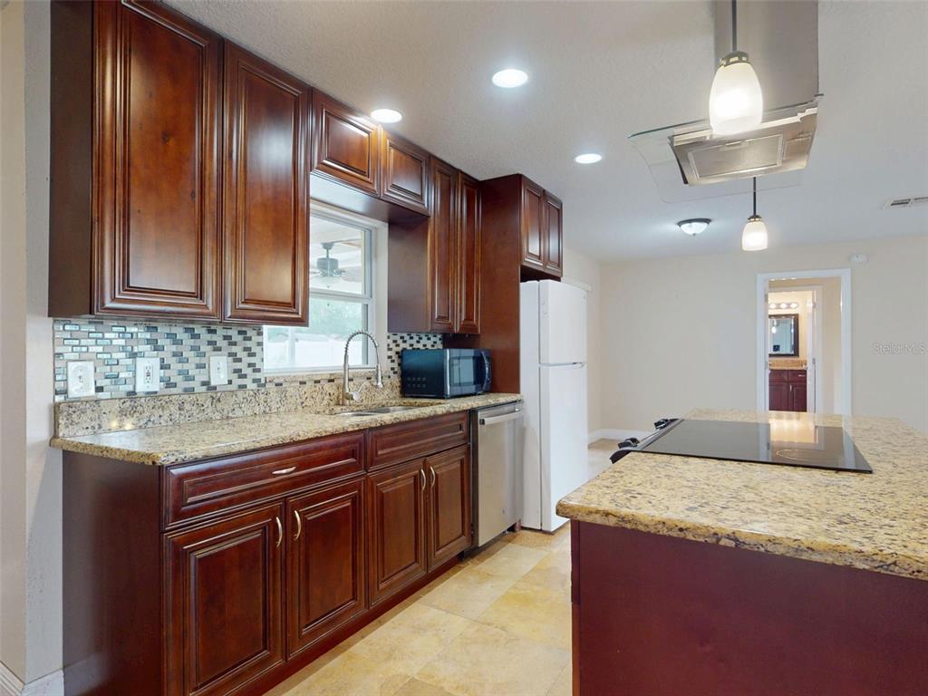 A kitchen features dark wood cabinets, granite countertops, a tiled backsplash, and a center island — 2125 E PARKTON DRIVE, DELTONA, FL
