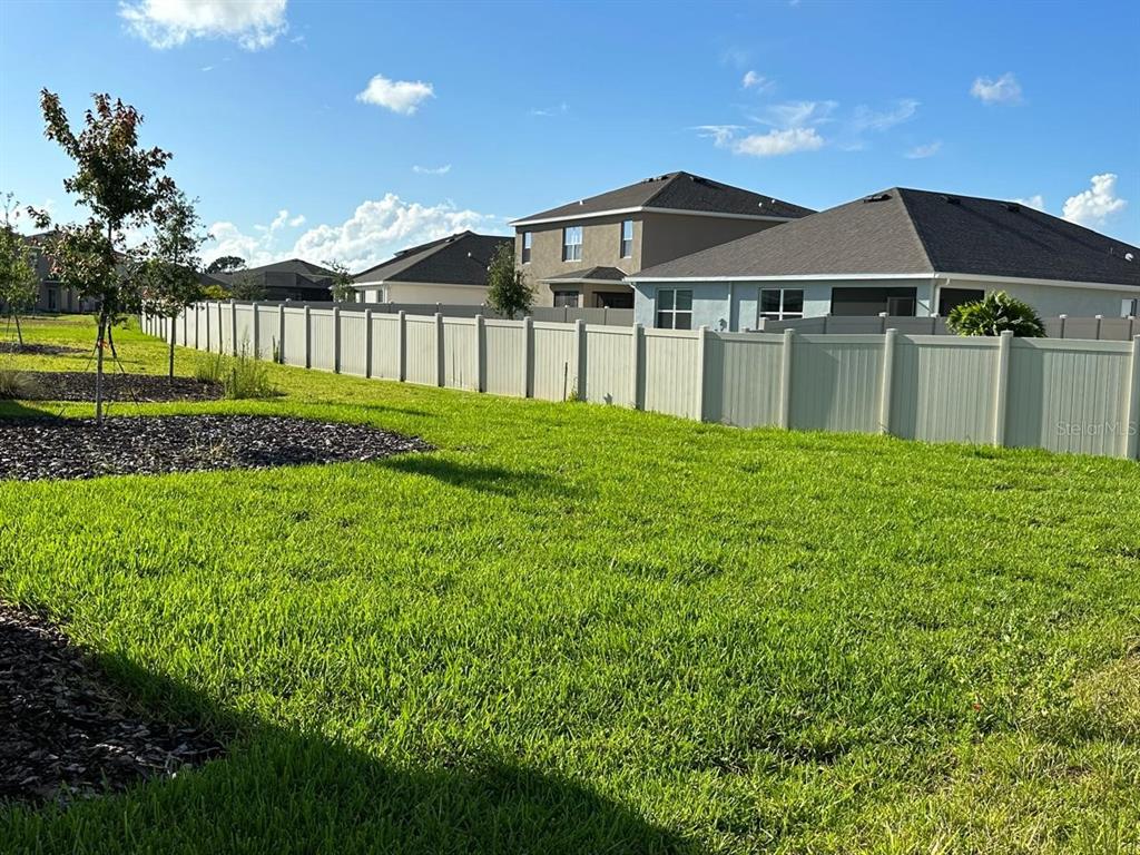 A grassy backyard features a tall vinyl fence and several suburban houses in the background — 12760 LATERAL ROOT DRIVE, SARASOTA, FL