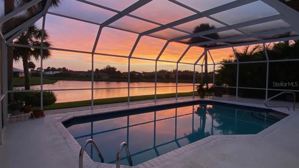 An aerial view shows a single-story house with a white roof, pool cage, and lakefront backyard — 1679 VALLEY DRIVE, VENICE, FL