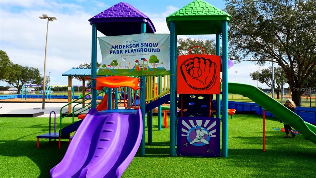 A colorful playground structure with slides and a baseball-themed sign sits on a green surface — 12515 LANGLEY DRIVE Lot 92, SPRING HILL, FL