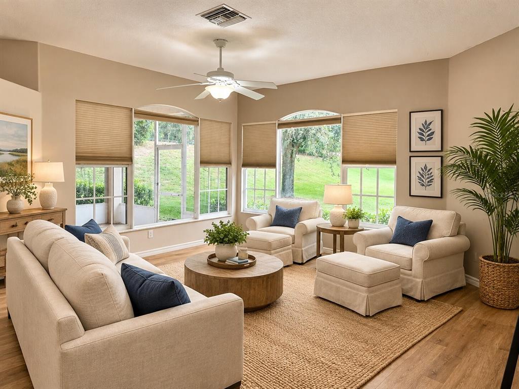 A living room features beige furniture, a round wooden coffee table, and large windows overlooking greenery — 39905 BAYVIEW DRIVE, LADY LAKE, FL