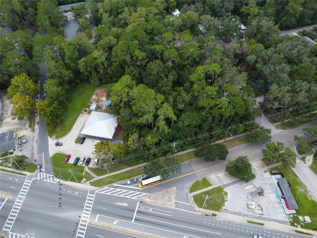 An aerial view shows a commercial building with a parking lot surrounded by dense trees — 1715 SE 4TH AVENUE, GAINESVILLE, FL