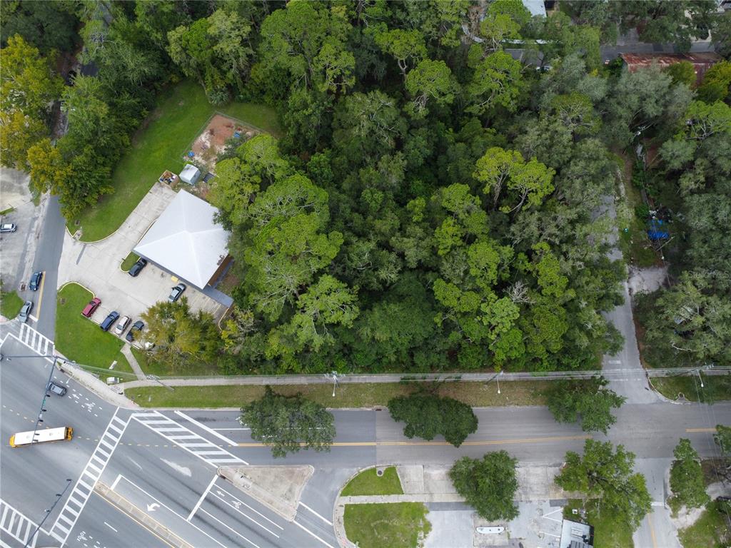 An aerial view shows a wooded lot adjacent to a building with a white roof — 1715 SE 4TH AVENUE, GAINESVILLE, FL