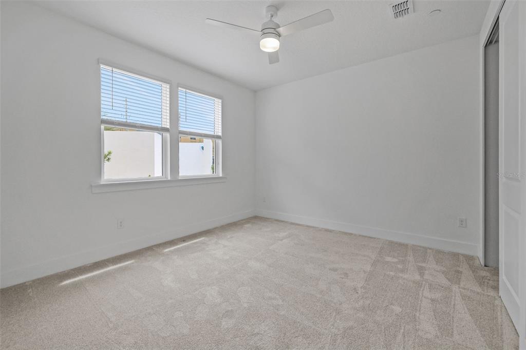 An empty bedroom features white walls, beige carpeting, a ceiling fan, and two windows — 1043 N 1ST AVENUE, JACKSONVILLE BEACH, FL