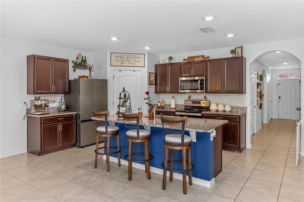 A kitchen features dark wood cabinets, granite countertops, a blue island with barstools, and tile flooring — 319 CHARLES DRIVE, DELAND, FL