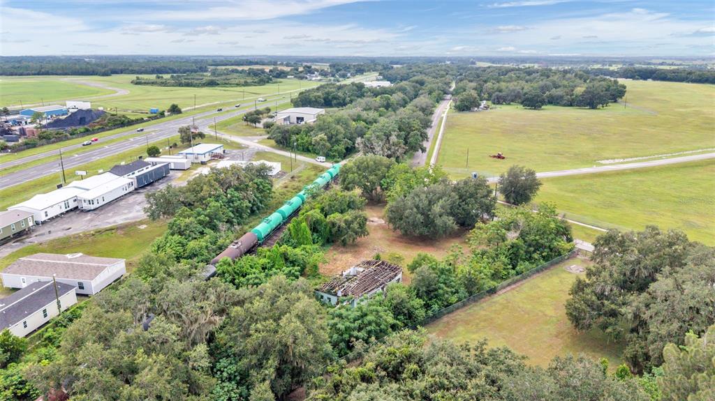 An aerial view shows a freight train passing through a rural area with nearby buildings — 3852 RADFORD ROAD, BARTOW, FL