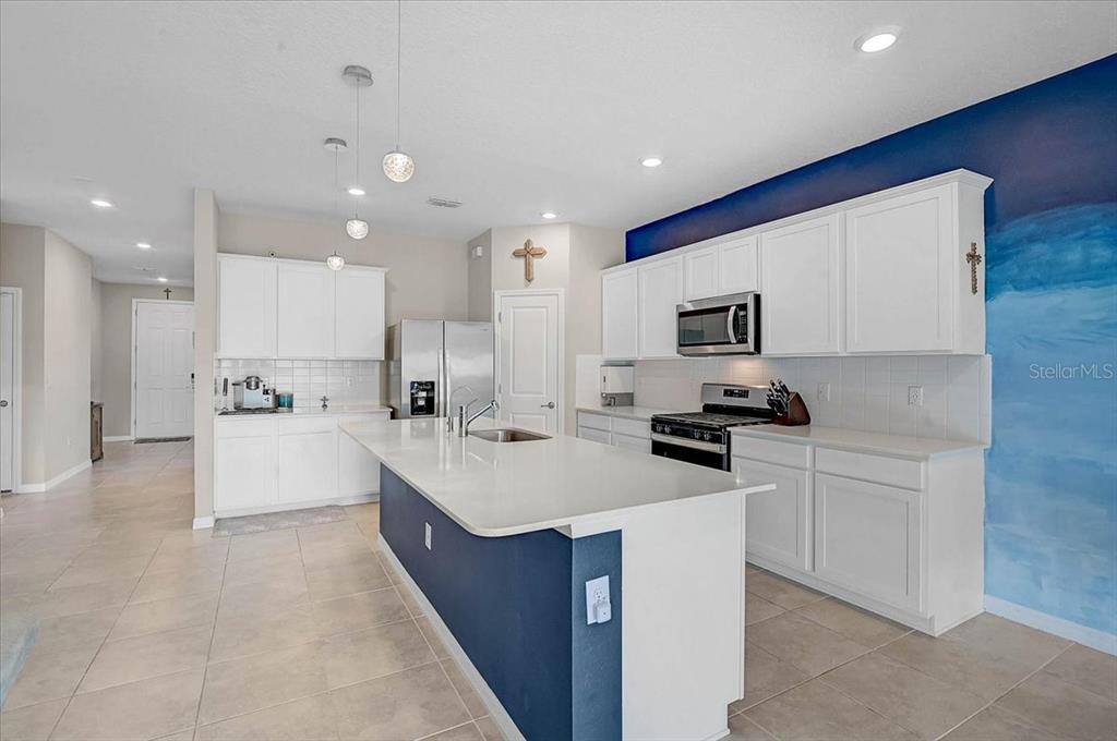 A kitchen features white cabinetry, a blue island with a white countertop, and tile flooring — 3110 61ST DRIVE E, ELLENTON, FL