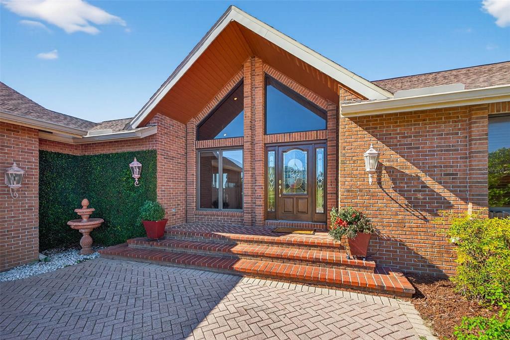 A brick house exterior features a gabled entryway with a glass-paneled door and steps — 36649 COVINGTON ROAD, DADE CITY, FL