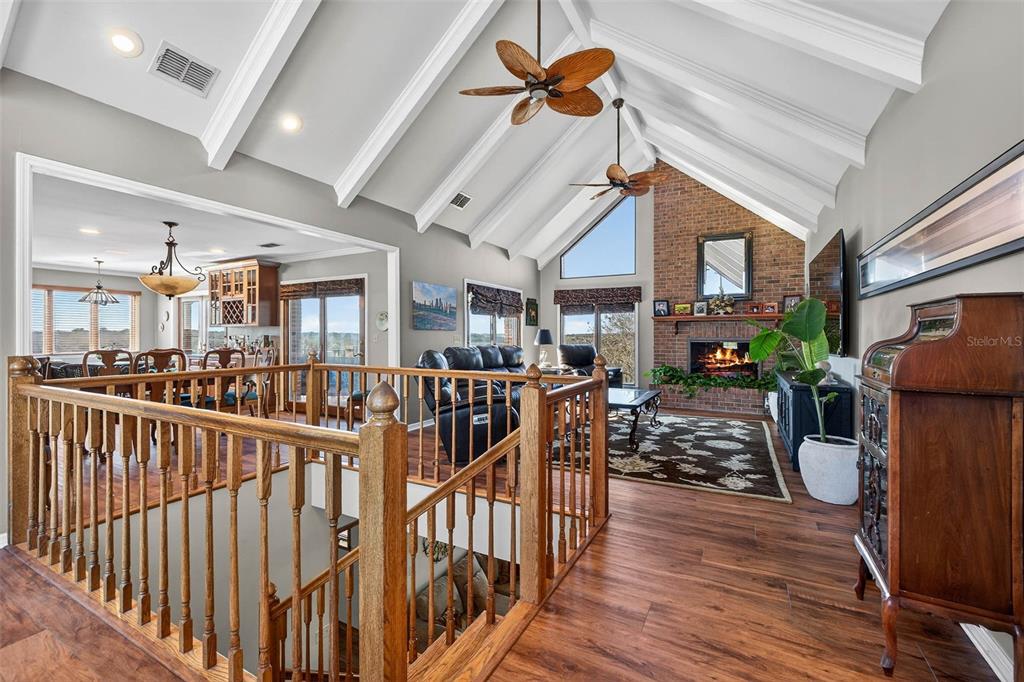 A living room with a vaulted ceiling, brick fireplace, and wooden staircase overlooking a lower level — 36649 COVINGTON ROAD, DADE CITY, FL