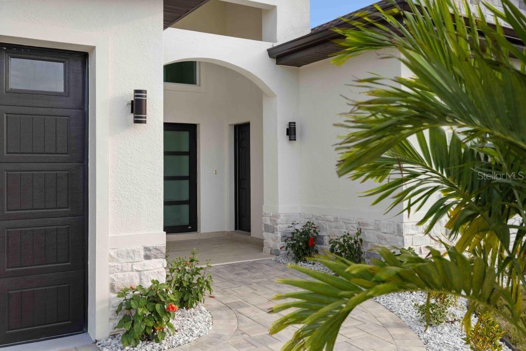 A modern home entrance features a stone-accented facade, a covered porch, and a palm tree — 38 LARK DRIVE, PLACIDA, FL