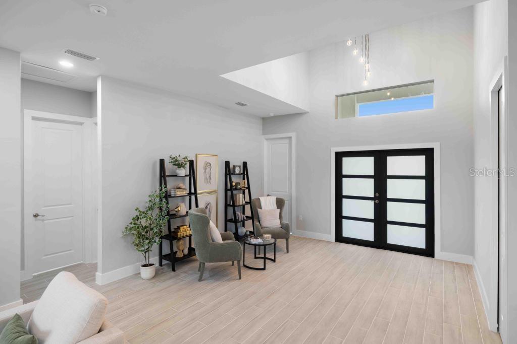 A bright living area features high ceilings, light wood-look tile flooring, and black-framed glass doors — 38 LARK DRIVE, PLACIDA, FL