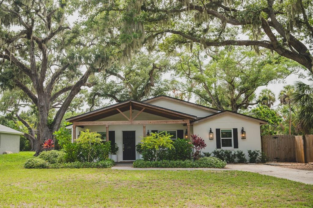 A single-story house with a covered front porch, white siding, and large oak trees — 216 18TH STREET E, BRADENTON, FL
