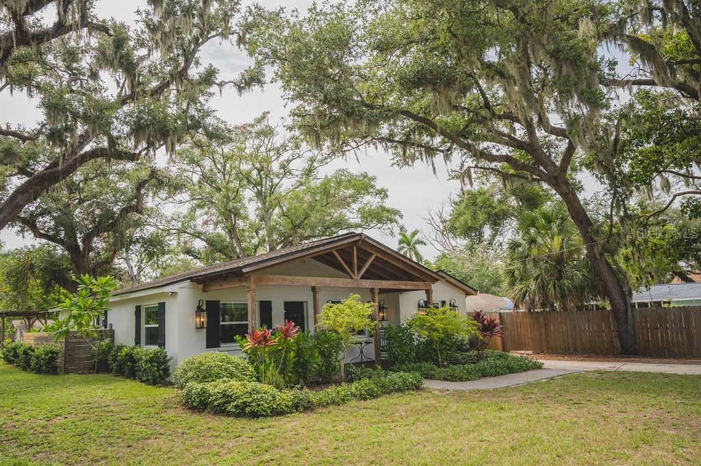 A single-story house with a wooden front porch sits under large trees with Spanish moss — 216 18TH STREET E, BRADENTON, FL